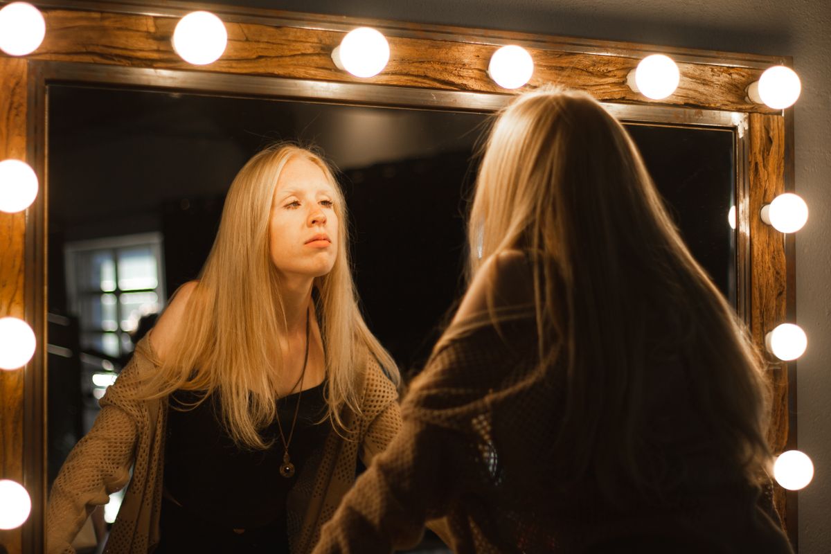Blonde woman studying mirror glow highlighting everyday psychological effects from sustained mirror fixation