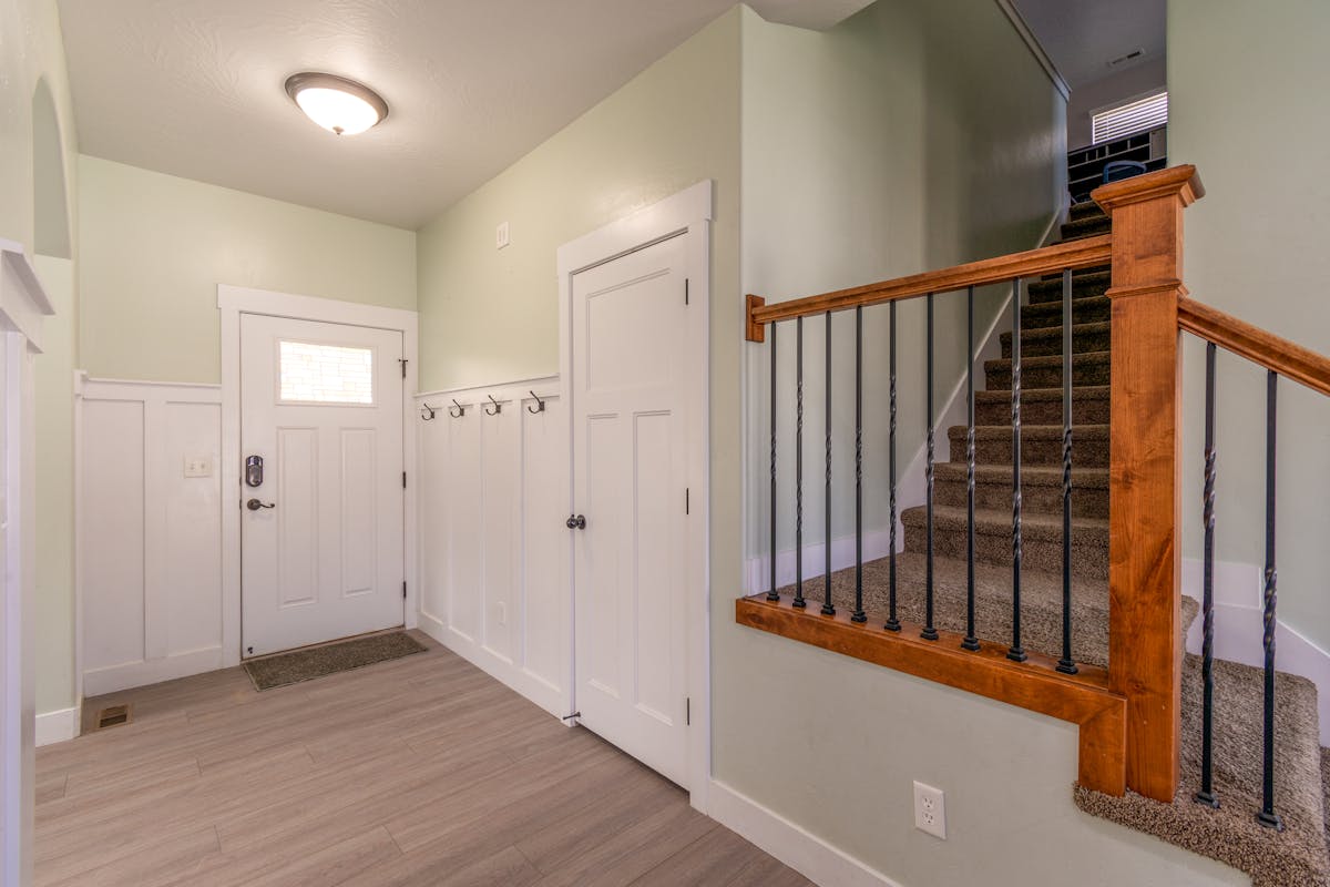 Bright entryway with wall-mounted coat hooks beside a white door, showing how to mount an entryway mirror with hooks
