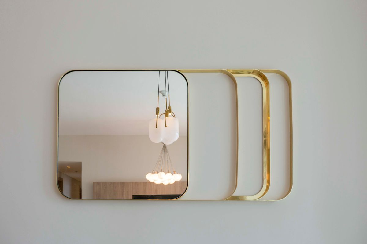 Gold-framed mirror illustrating living room mirror frame and finish ideas Wall mirror with a gold frame reflecting contemporary lighting, illustrating mirror frame and finish ideas