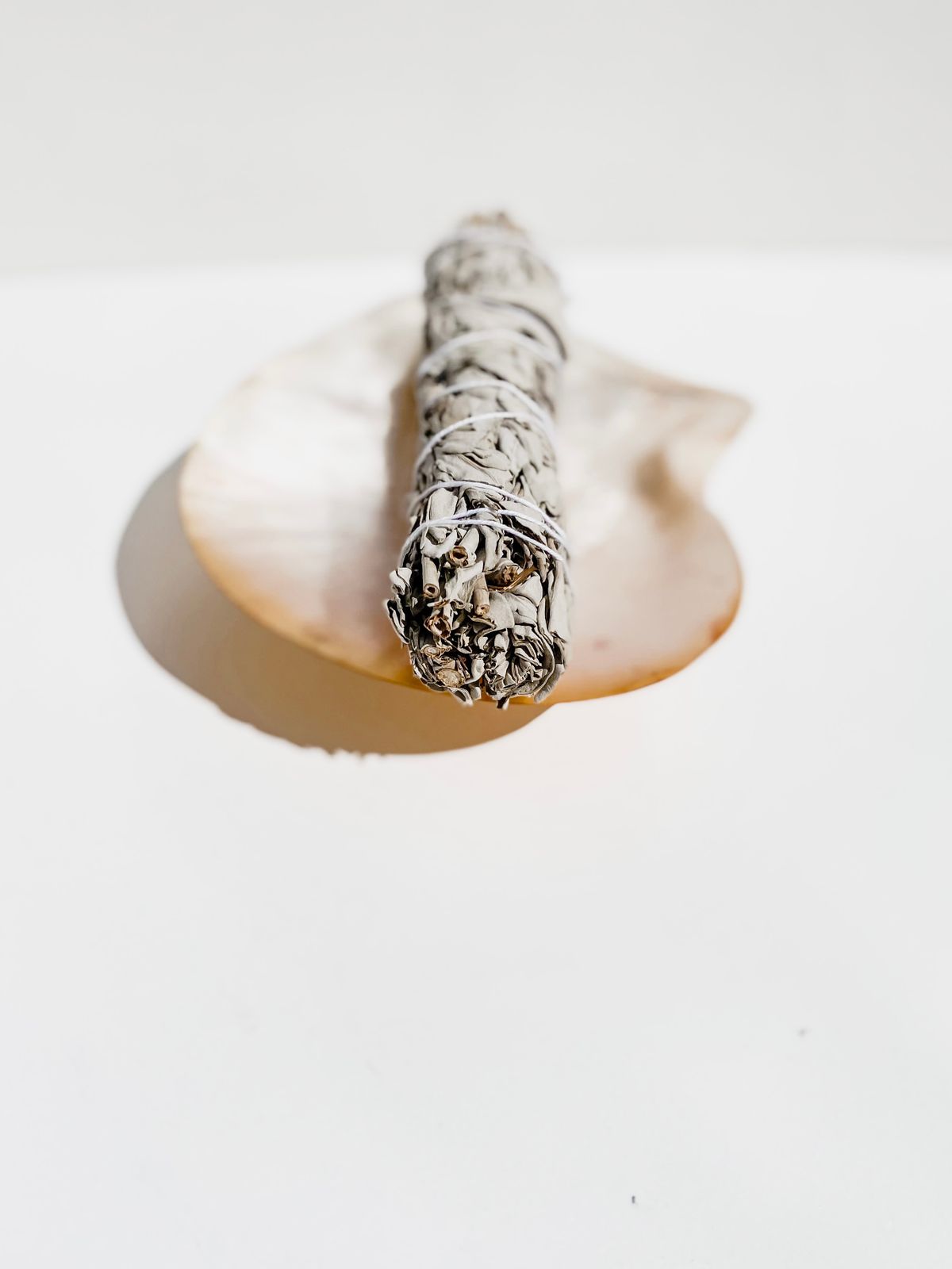 Dried sage smudge bundle and cleansing tools on neutral surface in soft daylight