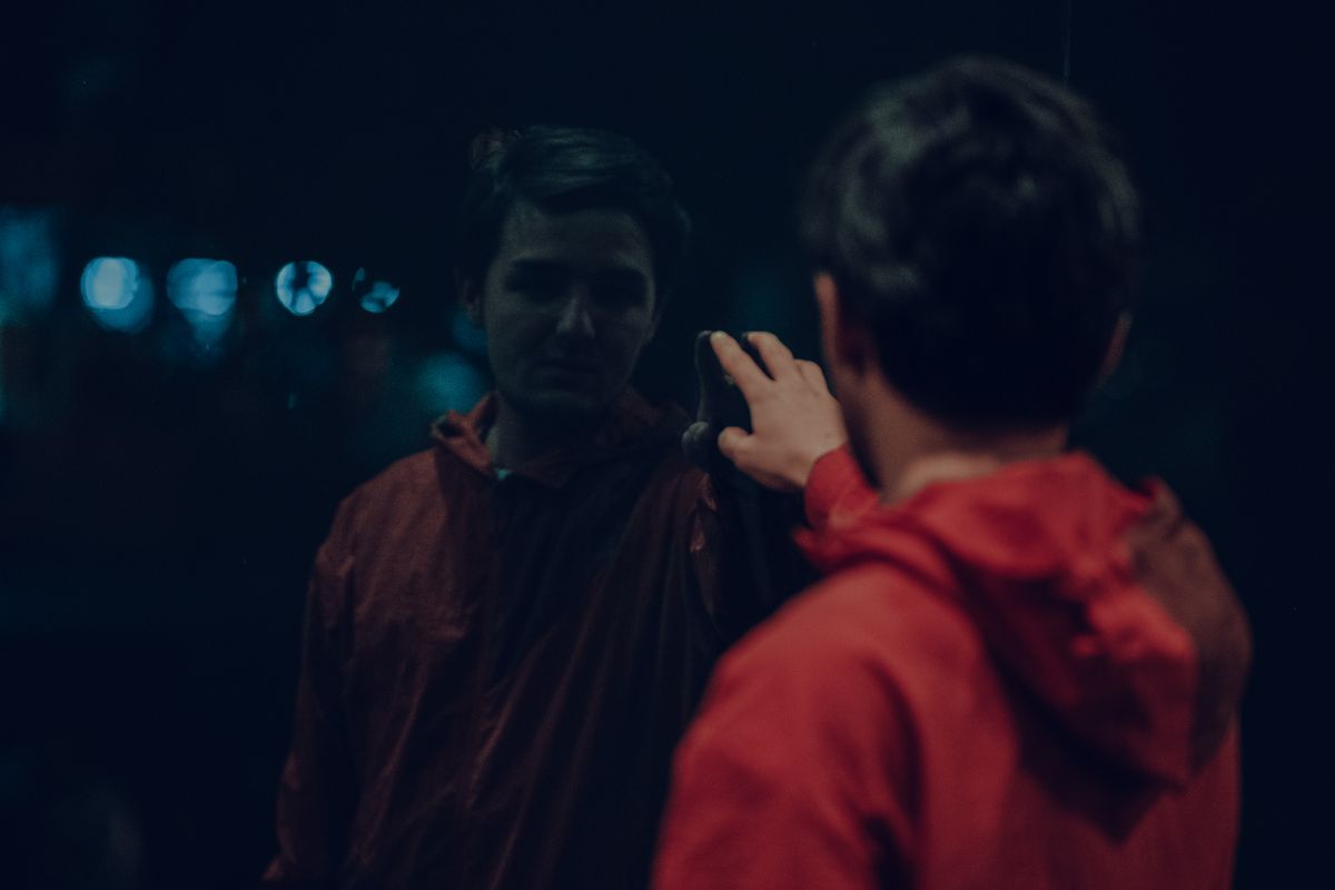 Person reaching toward dark reflective panel at night suggesting tactile curiosity across mirrored boundary