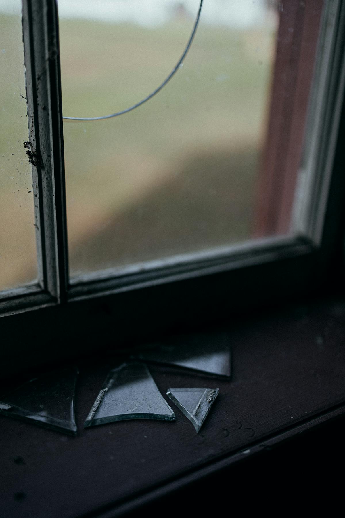 Broken window glass shards suggesting emotional rupture and warning themes in dreams Moody broken window glass with scattered shards on sill suggesting warning and emotional rupture in dreams