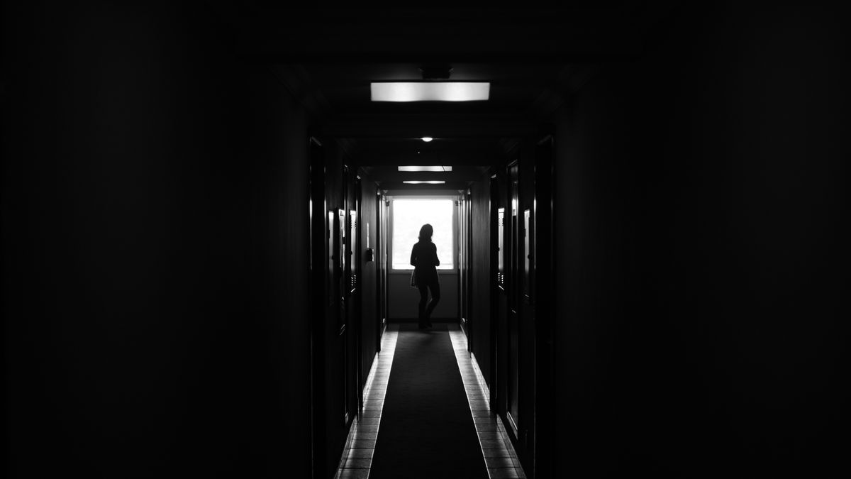 A dramatic silhouette of a lone figure standing in a dark hallway representing the threatening or distorted presence that can appear in mirror dreams