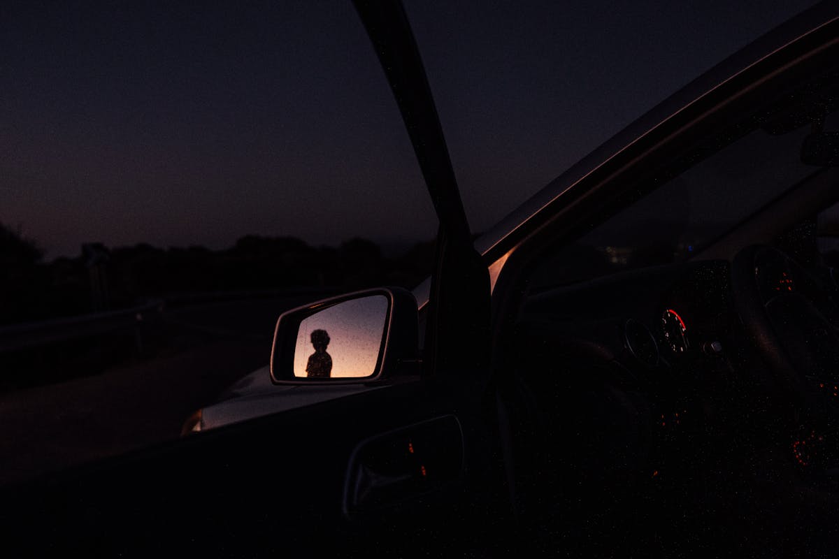 Nighttime urban glow reflected in vehicle side mirror illustrating liminal mirror symbolism between darkness and doubled city lights