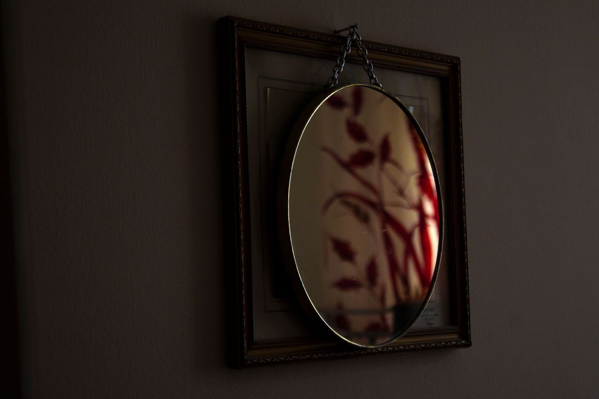 Oval mirror on wall reflecting abstract art in a moody dimly lit interior