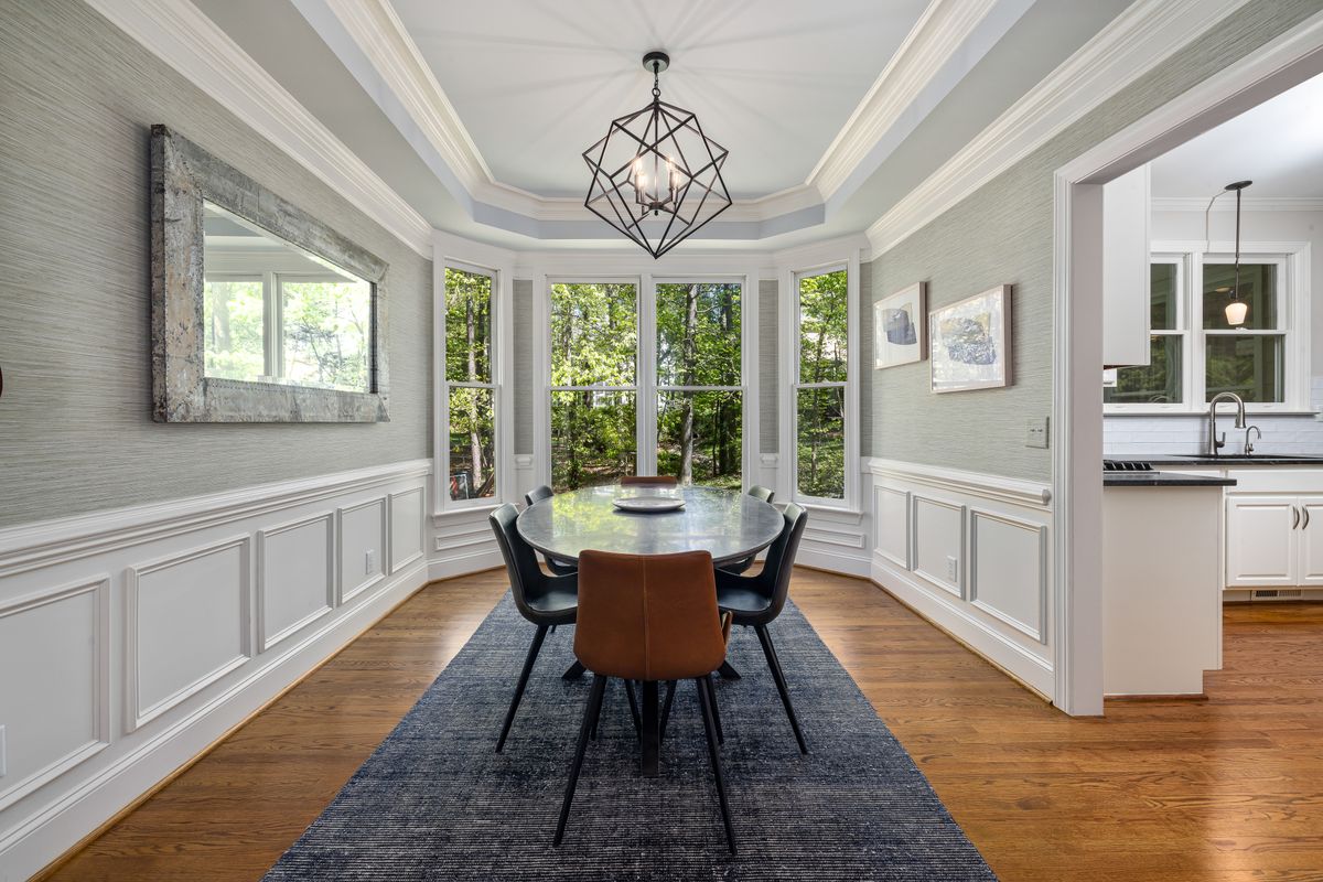 Bright dining room where a mirror reflects window light, showing the benefit of mirrors for a dining room Dining room with large windows and a wall mirror reflecting daylight, showing why mirrors for a dining room brighten the space