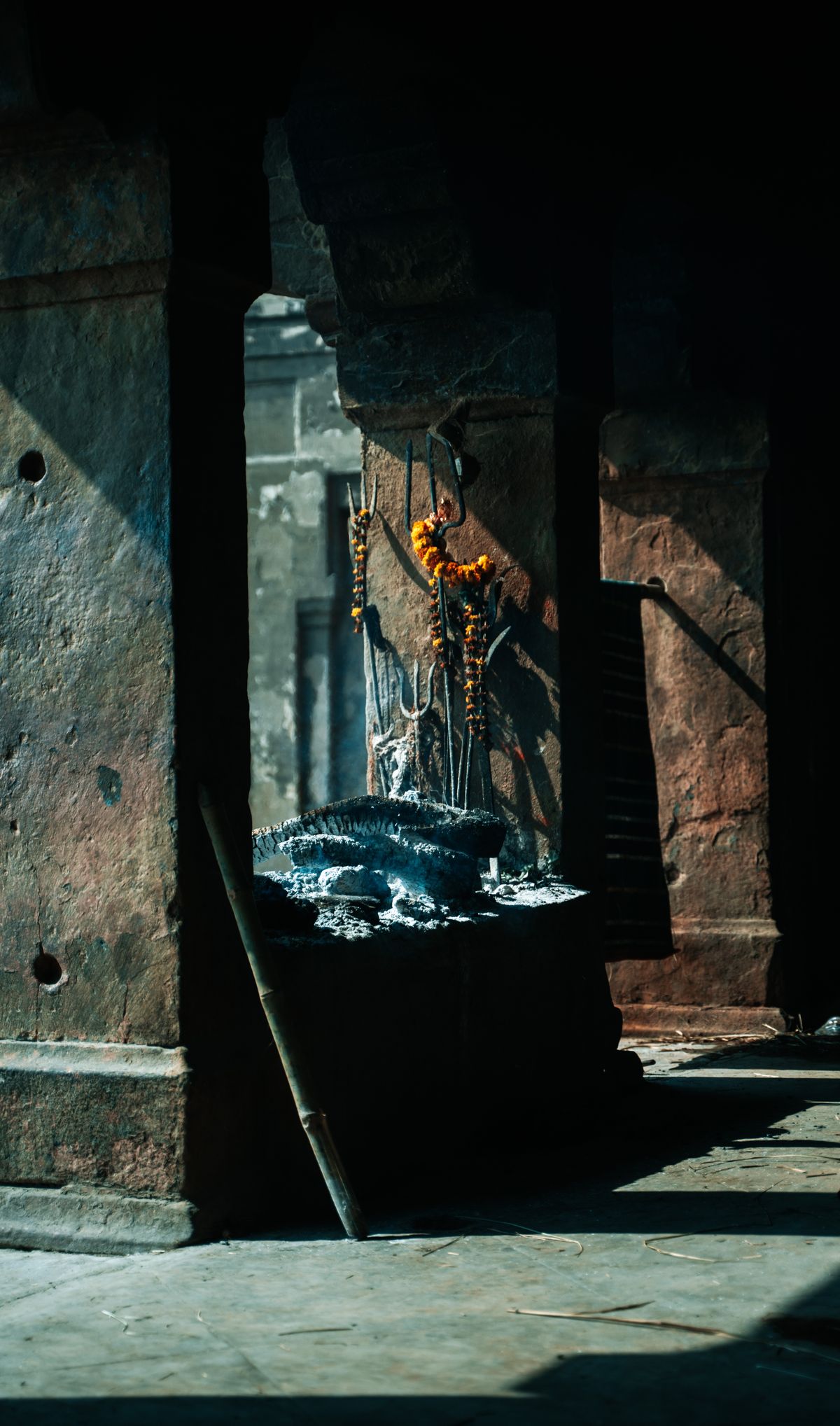 Ancient temple interior in Varanasi with garlands and ash suggesting the sacred context of Darpana offerings Atmospheric view inside an ancient temple with ash remnants and marigold garlands in Varanasi evoking the sacred space where Darpana rituals are performed