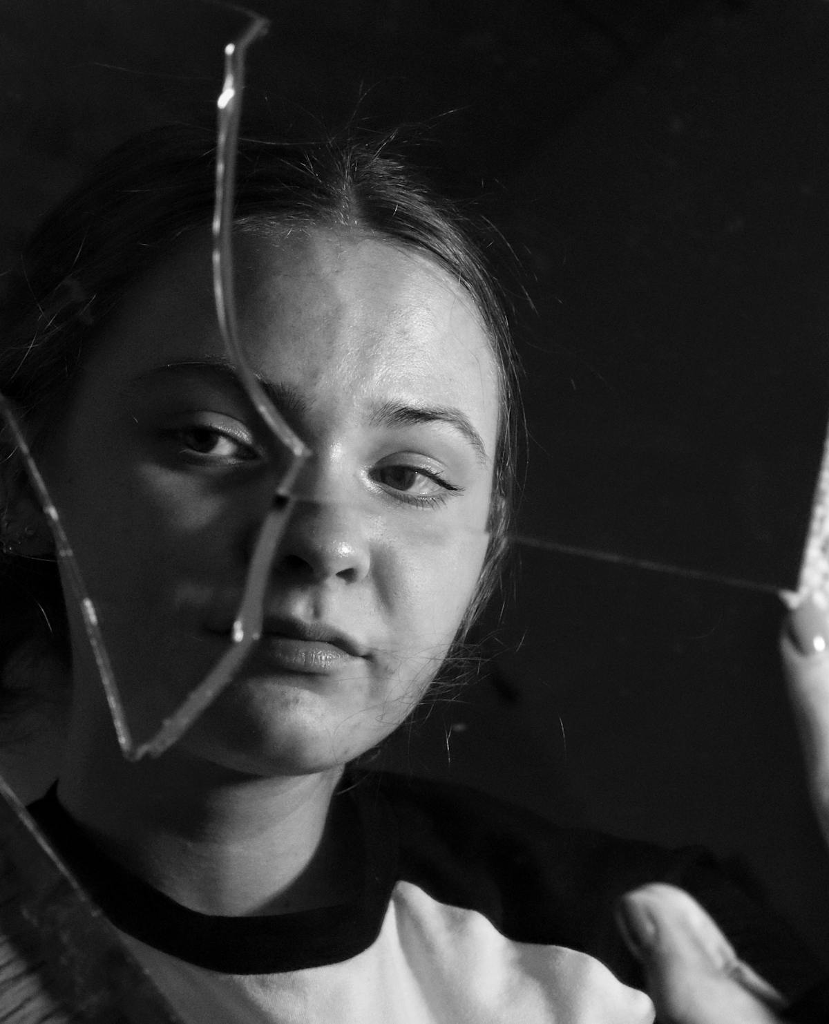 Person eyes close up reflected in hand held broken mirror shard outdoors with yellow flowers