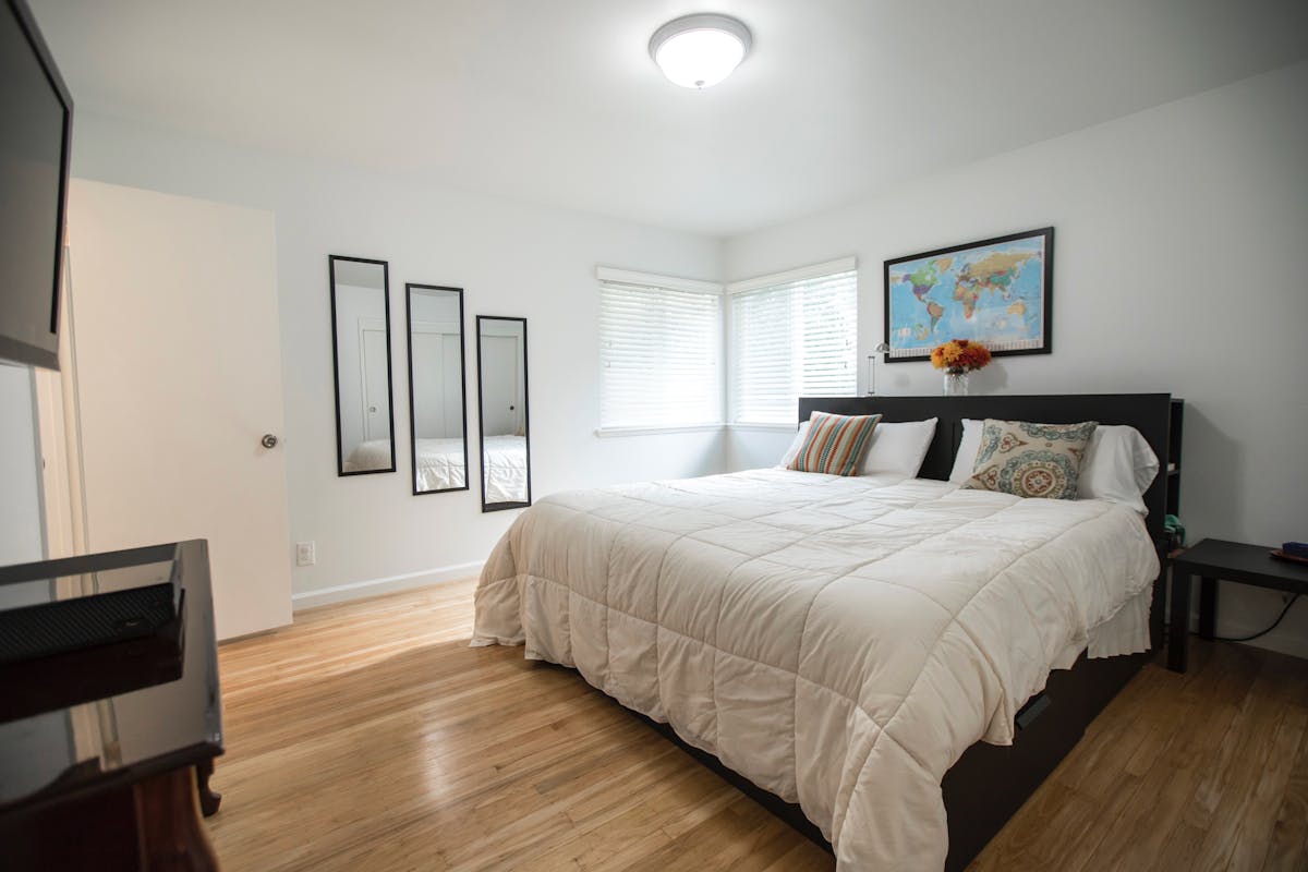 Bedroom with wood floors and a large mirror illustrating a full-length wood mirror Bright bedroom with wood floors, a large bed, and mirrors, illustrating a full-length wood mirror