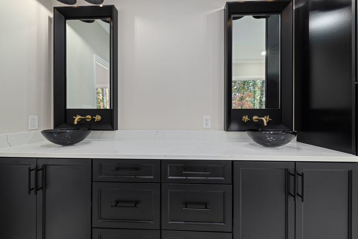 Black cabinets with gold hardware illustrating how to pair black mirror decor with warm metallics Bathroom with black cabinets, vessel sinks, and gold hardware, illustrating black mirror decor paired with metallics