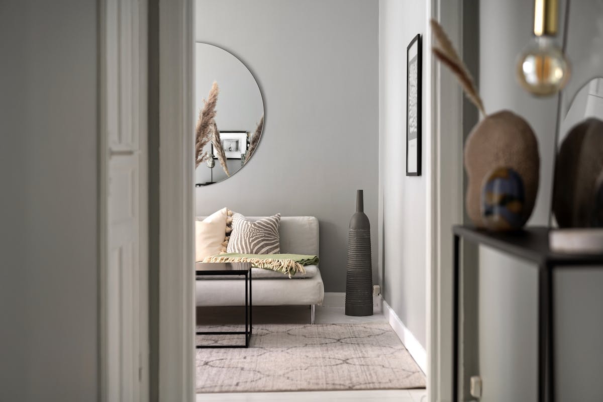 Living room with a round mirror above a sofa illustrating round mirror placement over furniture Cozy living room with a sofa, round mirror, and elegant furnishings, illustrating round mirror placement over a sofa