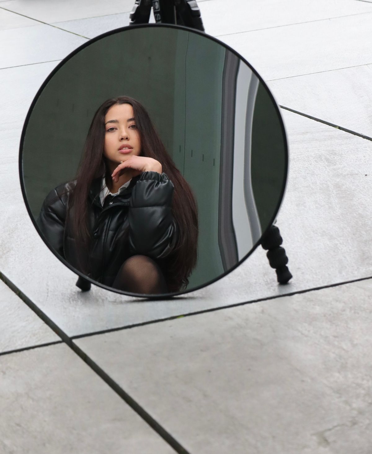 Urban sidewalk round mirror reflection portrait Young woman reflected in round mirror on urban sidewalk suggesting public identity and self-presentation themes