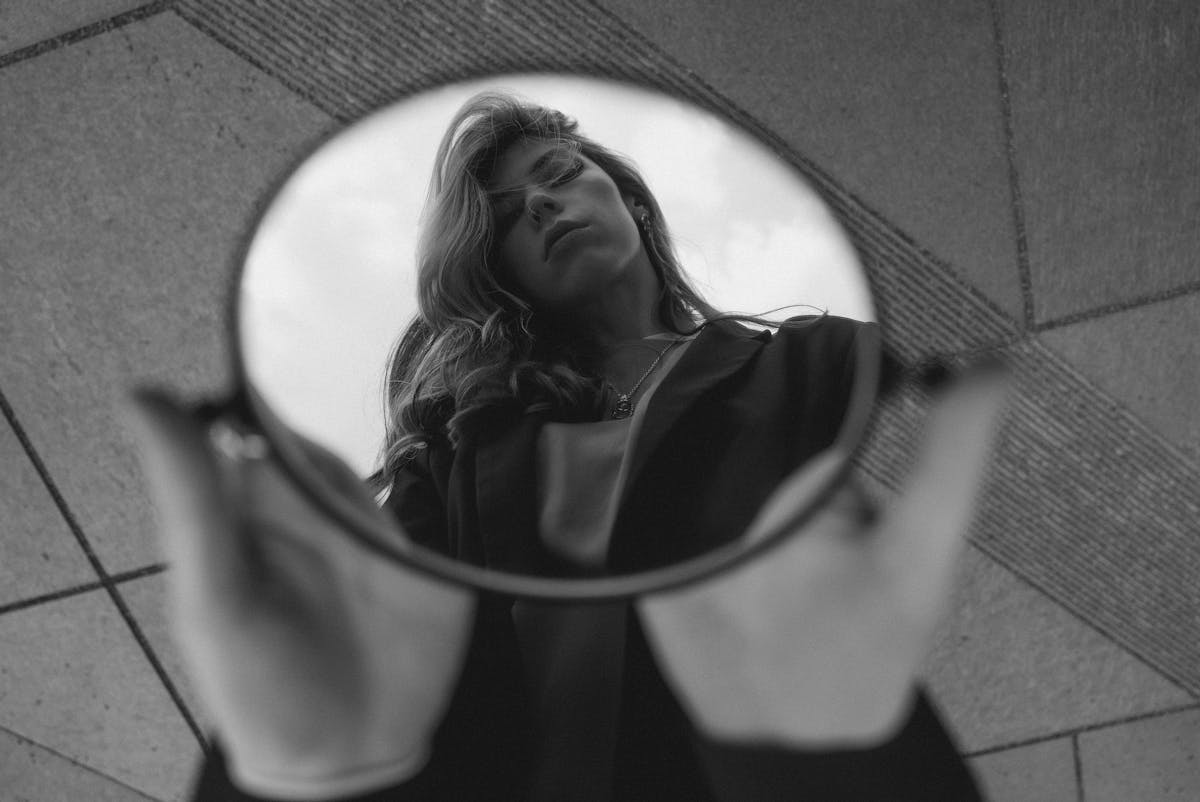 Black and white artistic photo of a woman reflected in a round mirror evoking the uncanny cultural layer behind the fear of mirrors