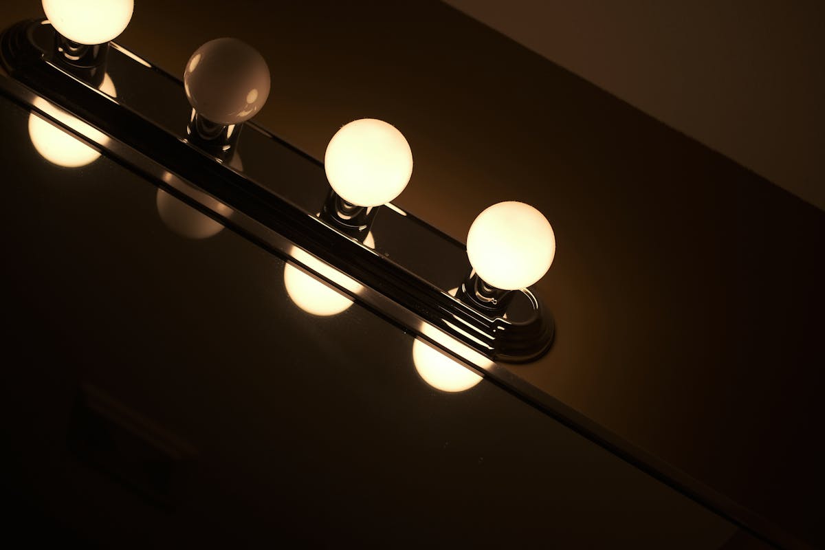 Vanity light fixture reflecting off a mirror illustrating the best vanity mirror lighting Contemporary vanity light fixture with glowing bulbs reflecting off a mirror, illustrating vanity mirror lighting