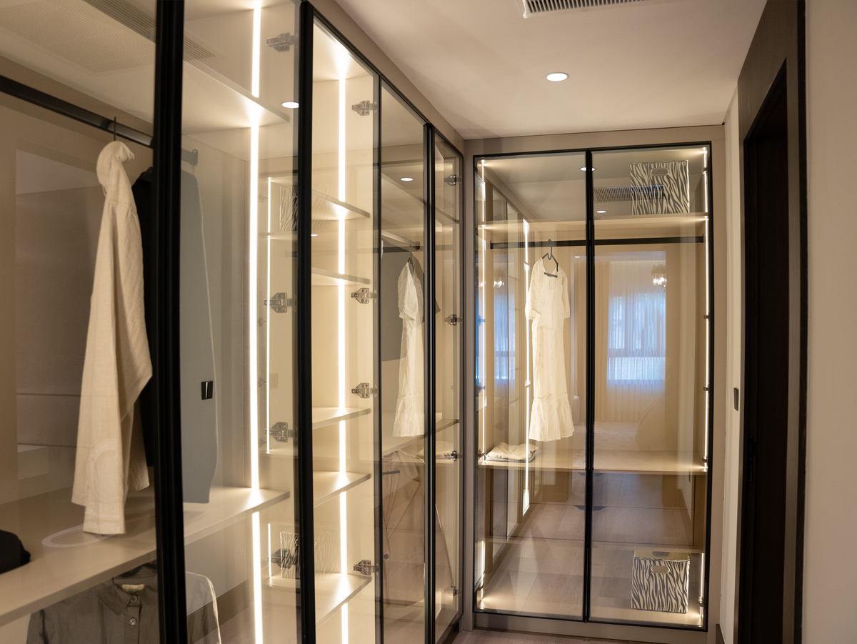 Walk-in wardrobe with integrated LED lighting illuminating mirrored doors Walk-in wardrobe with glass doors and integrated LED lighting illuminating a mirrored wardrobe