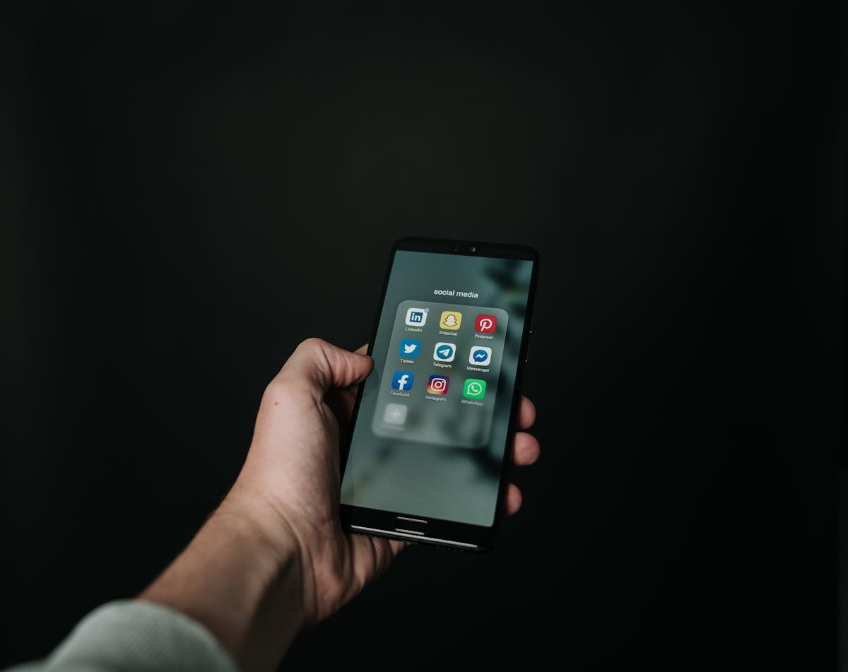 Hand holding smartphone showing glowing screen in dim setting suggesting late night social scrolling