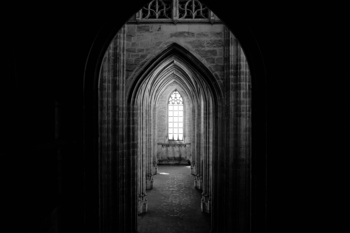 Monochrome interior of a vaulted historic corridor leading toward a distant window