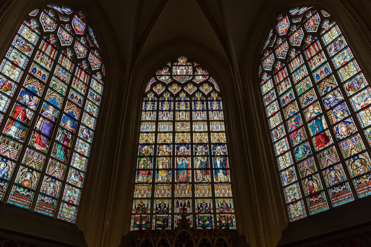 Intricate stained glass windows in a Gothic style church in Brussels representing the indirect beauty of seeing God through the glass darkly of human understanding