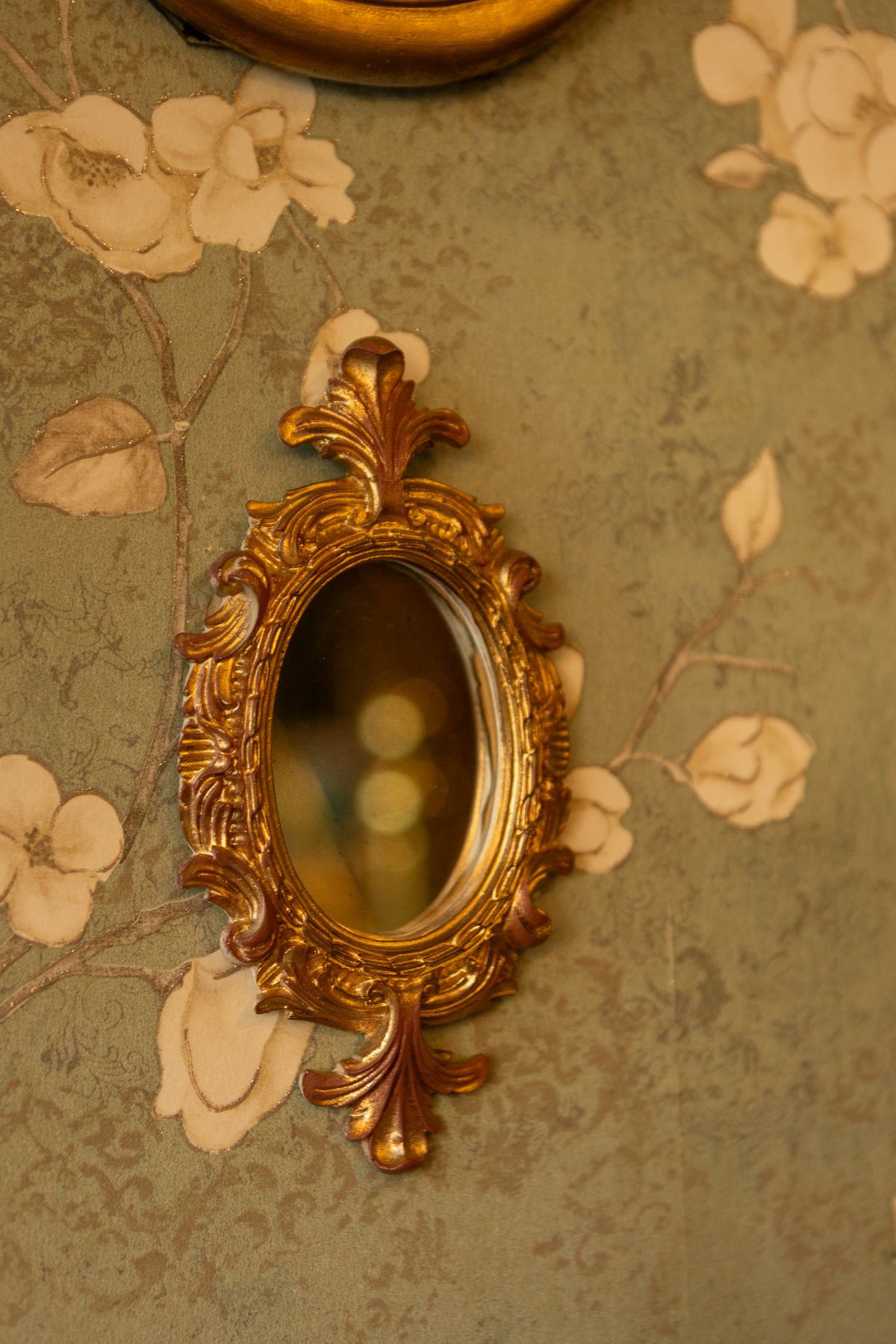 Ornate antique gold mirror on floral wallpaper in interior setting Antique ornate gold mirror on floral wallpaper evoking cultural history of mirrors beauty and superstition
