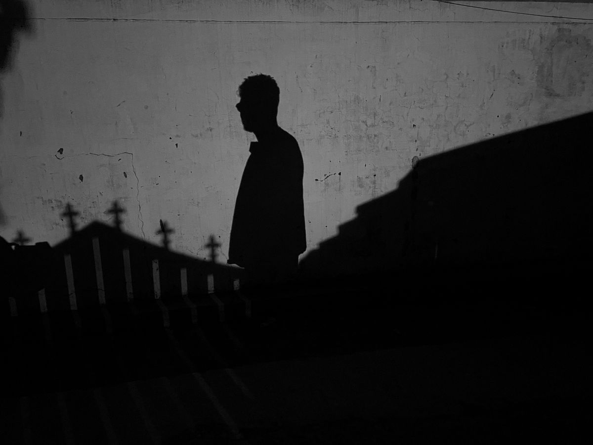 Dark silhouette of a person against a textured wall at twilight representing the shadow self confronted in black mirror scrying