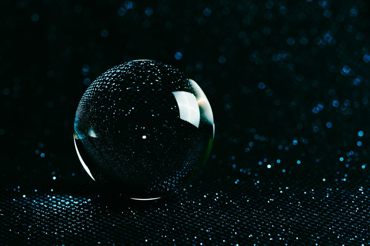 Glowing glass sphere with water droplets on a deep black studio background