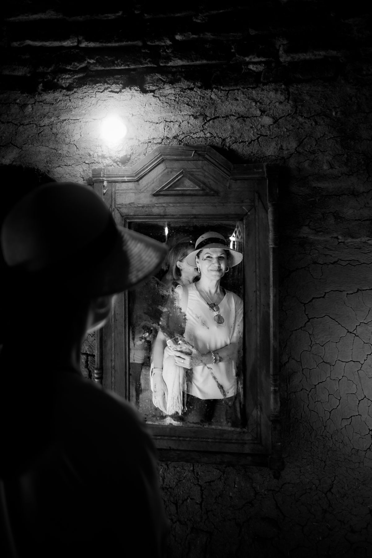 Black and white portrait of a woman in a hat looking into a vintage mirror in a thoughtful atmosphere