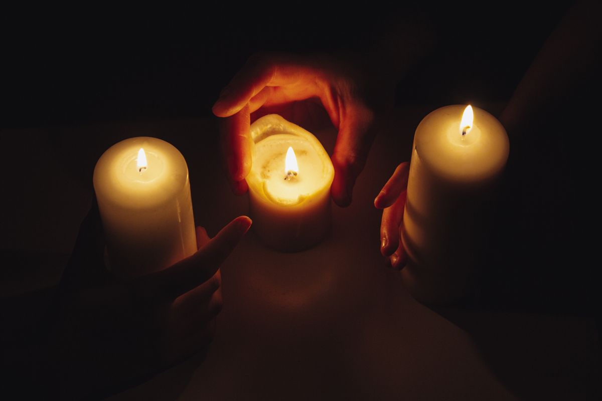 Hands cupping small lit candles in a dark intimate meditation setting