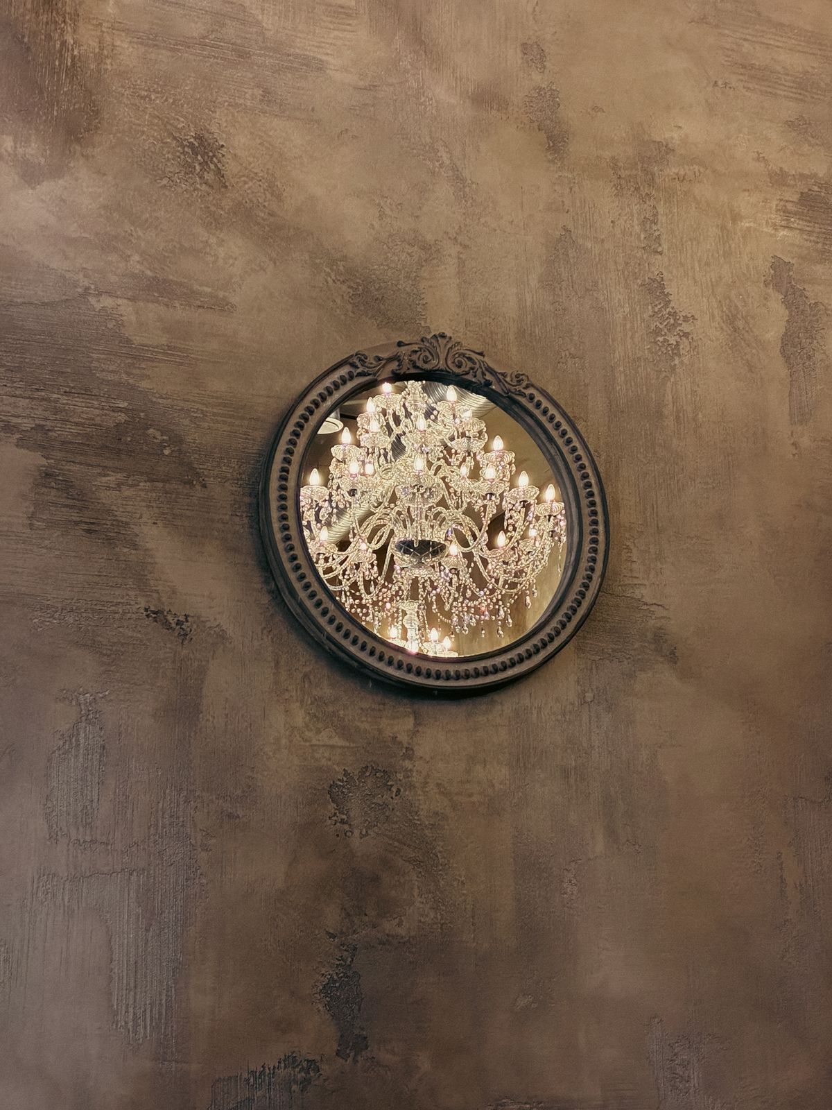 Chandelier reflection in an ornate round interior mirror Round decorative mirror reflecting a crystal chandelier on textured wall suggesting inner light and reflection symbolism