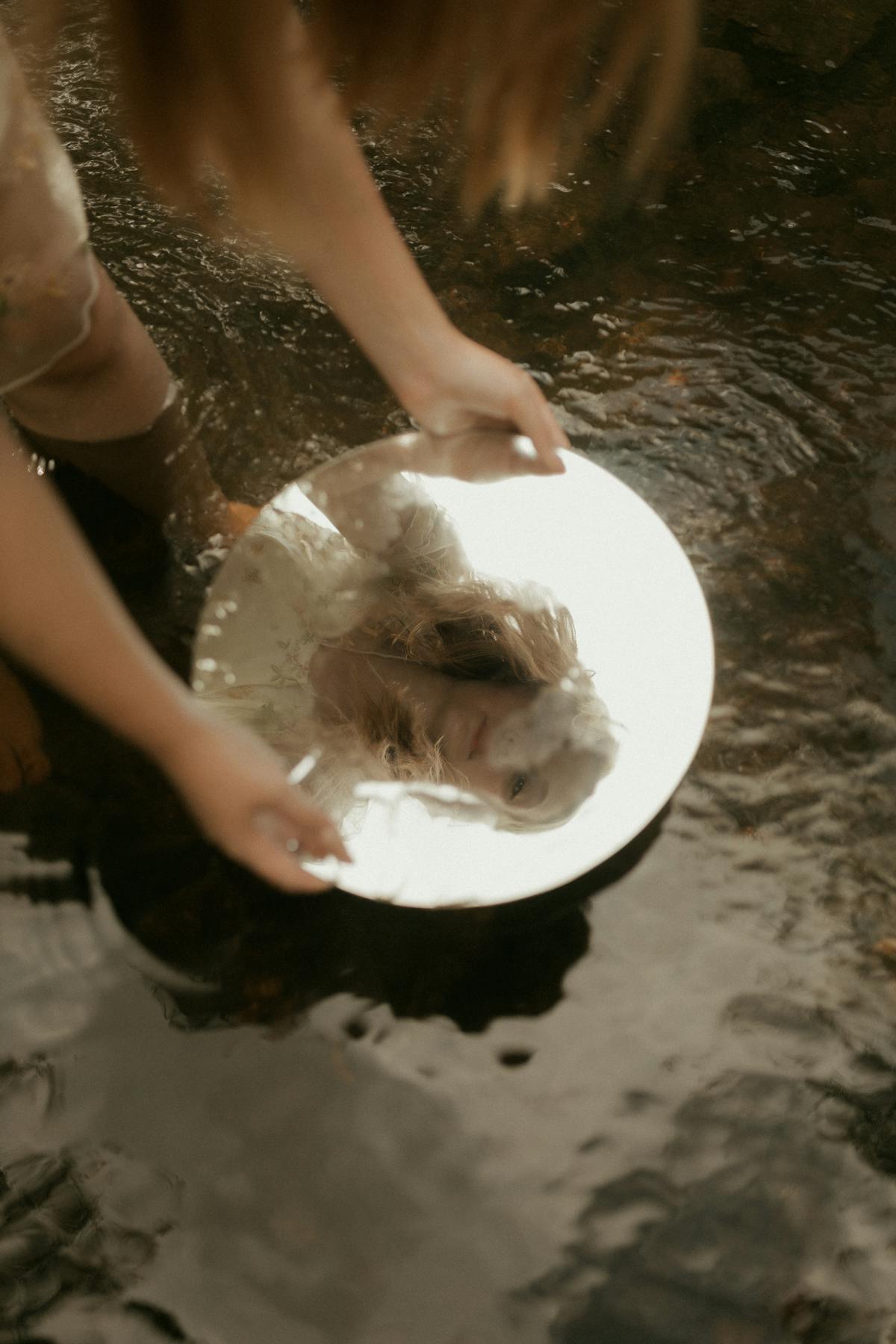 Dreamlike reflection of a woman in a circular mirror placed in water representing the recurring mirror dream meaning and persistent self-image questioning