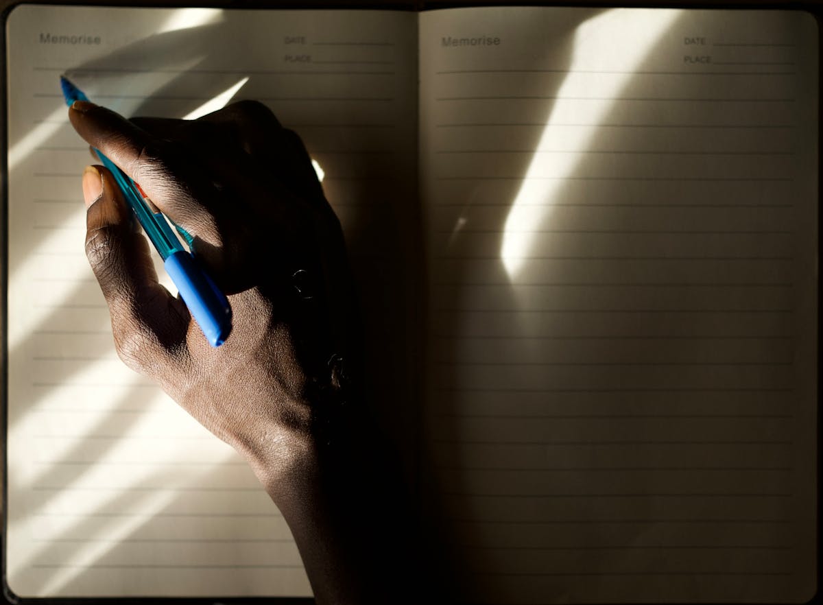 A hand writing in a journal illuminated by soft natural morning light representing the practice of dream journaling and reflection after meaningful dreams