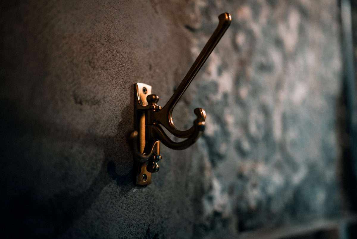 Close-up of a brass coat hook mounted on a textured wall, showing hook quality to look for in an entryway mirror with hooks