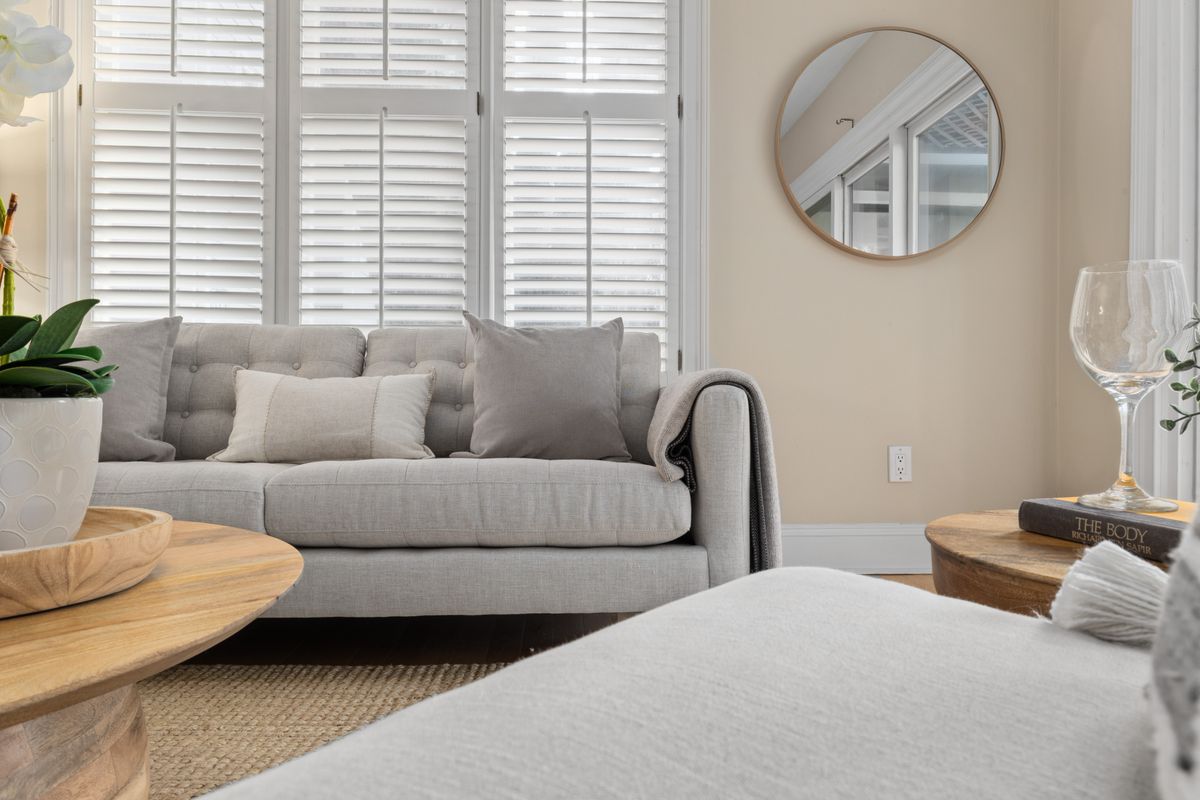 Round mirror sized to a sofa illustrating mirror over sofa sizing rules Light grey sofa with a round wall mirror above it in a bright living room, illustrating mirror over sofa sizing