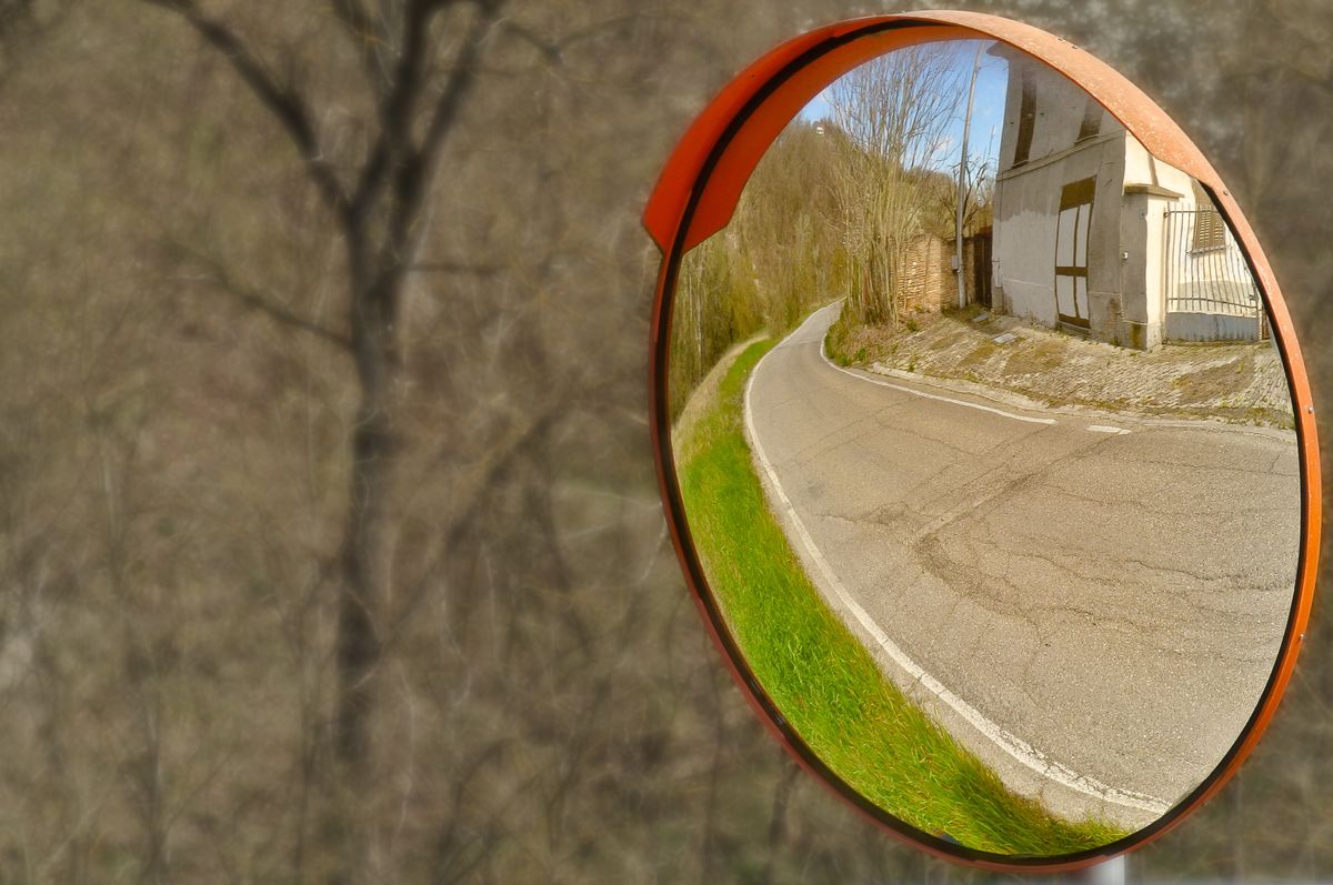 Convex mirror showing a wide-angle view of a curved rural road demonstrating how convex surfaces always produce diminished virtual images with a broader field of view than plane mirrors