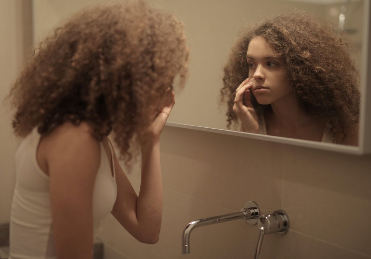 A young person examining their face closely in a bathroom mirror reflecting the contemplation and self-scrutiny common in the fear of mirrors