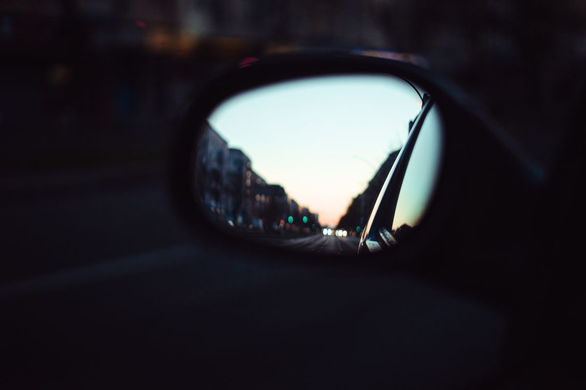 Twilight city avenue mirrored inside automotive rear surface illustrating doubled worlds symbolism