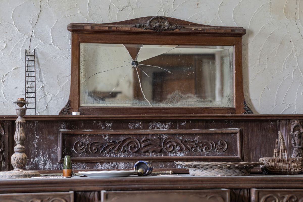 Antique cracked mirror on rustic sideboard evoking mirror superstition history and folk belief Antique wooden sideboard with cracked mirror in rustic interior linking folk beliefs and age of mirrors