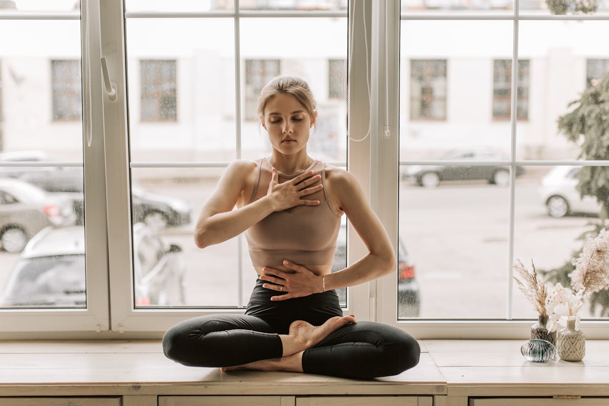 A woman practising calm breathing and meditation by a large bright window representing grounded spiritual practices that support recovery from the fear of mirrors