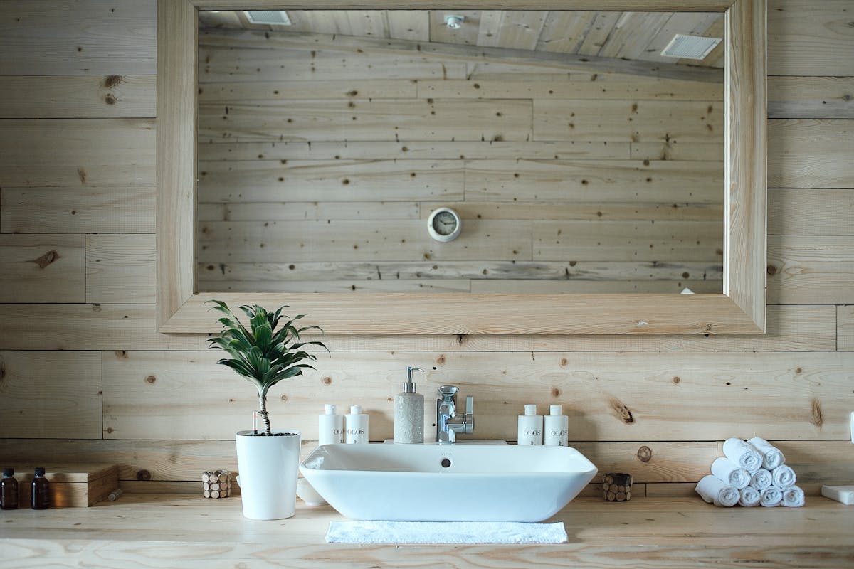 Bathroom with wooden walls and a framed mirror illustrating wood mirror frames in a humid room Contemporary bathroom with wooden walls and a large mirror above the sink, illustrating wood mirror frames in a bathroom