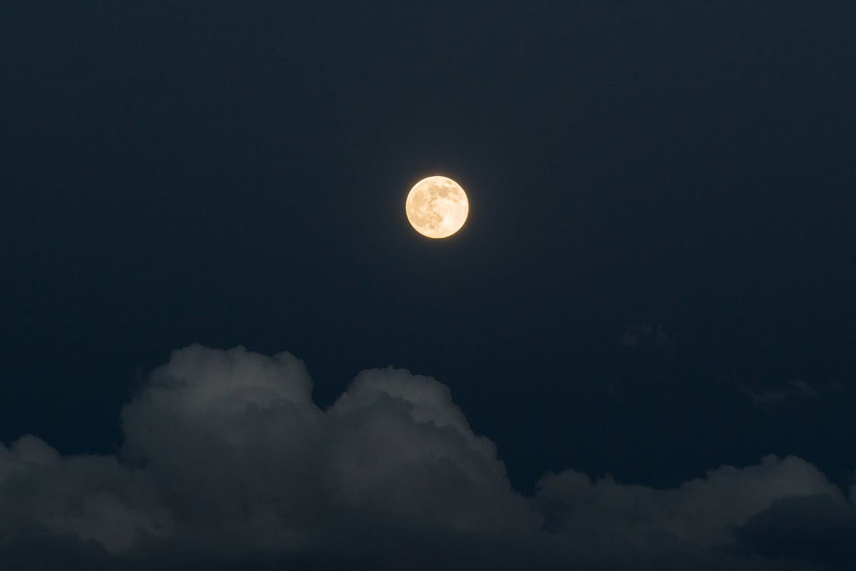Full moon glowing above thin clouds in a deep blue night sky