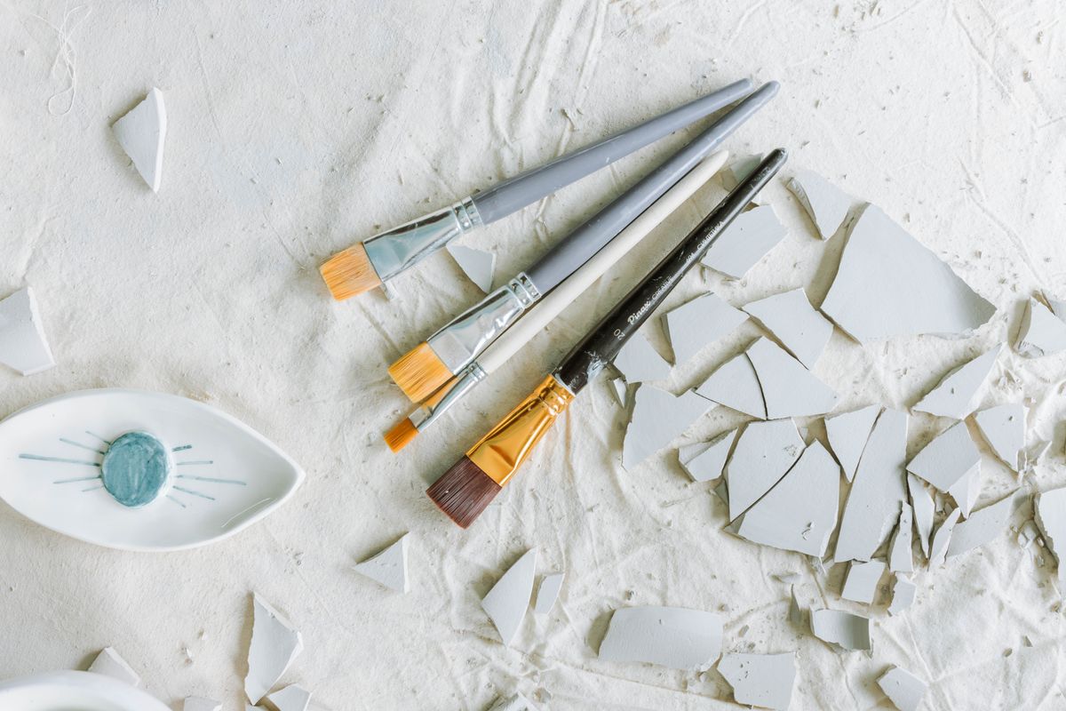Broken ceramic shards beside paint brushes evoking kintsugi repair and the broken mirror spiritual meaning of transformation across cultures