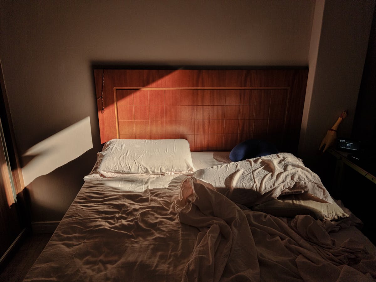 Sunlit bed with a wooden headboard in a warm bedroom, illustrating orienting the bed for feng shui sleeping direction
