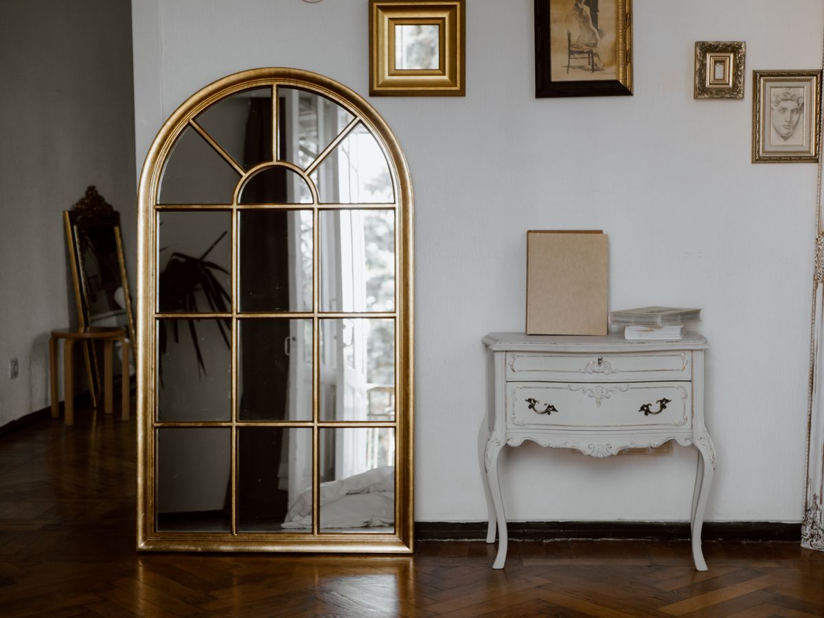 Arched gold mirror illustrating shapely living room mirror ideas Vintage-style interior with a gold arched mirror above a console, illustrating round and arched living room mirrors