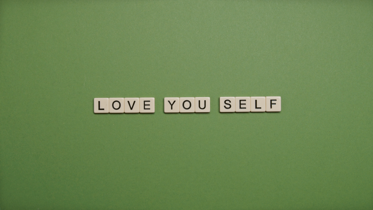 Bright letter tiles spelling out Love You Self arranged on a vivid green background representing self-love and personal affirmation