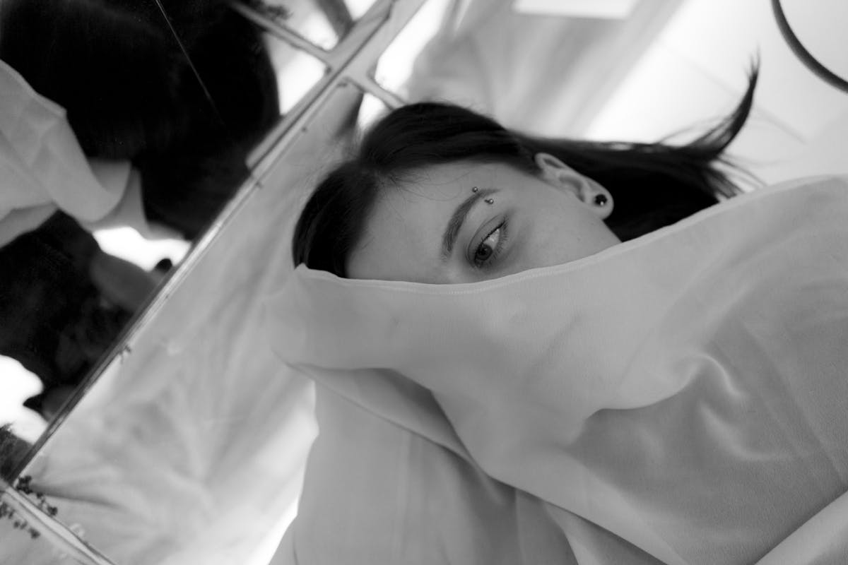 Black and white woman in a veil lying on a mirror, evoking the dreamlike symbolic quality of mirrors in the subconscious and the meaning of mirrors in dreams