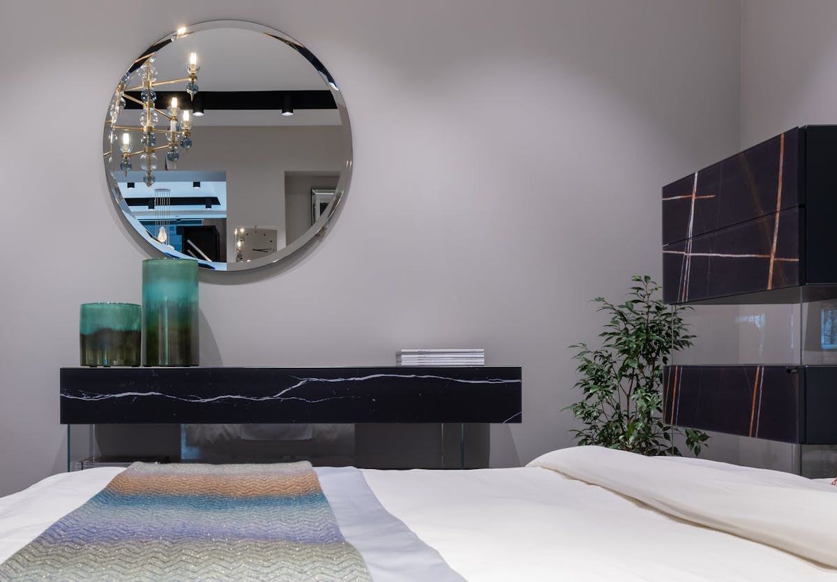 Round mirror above a bed demonstrating the best mirror shape and size over a bed Round mirror mounted on the wall above a bed showing the best mirror shape above a bed