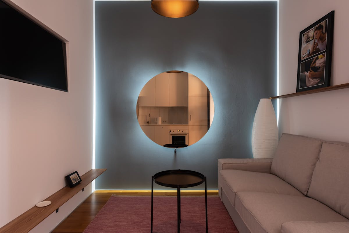 Round mirror bouncing light in a small living space illustrating feng shui mirror use Small living area with a round mirror on a bright wall reflecting light, illustrating feng shui mirrors in small spaces
