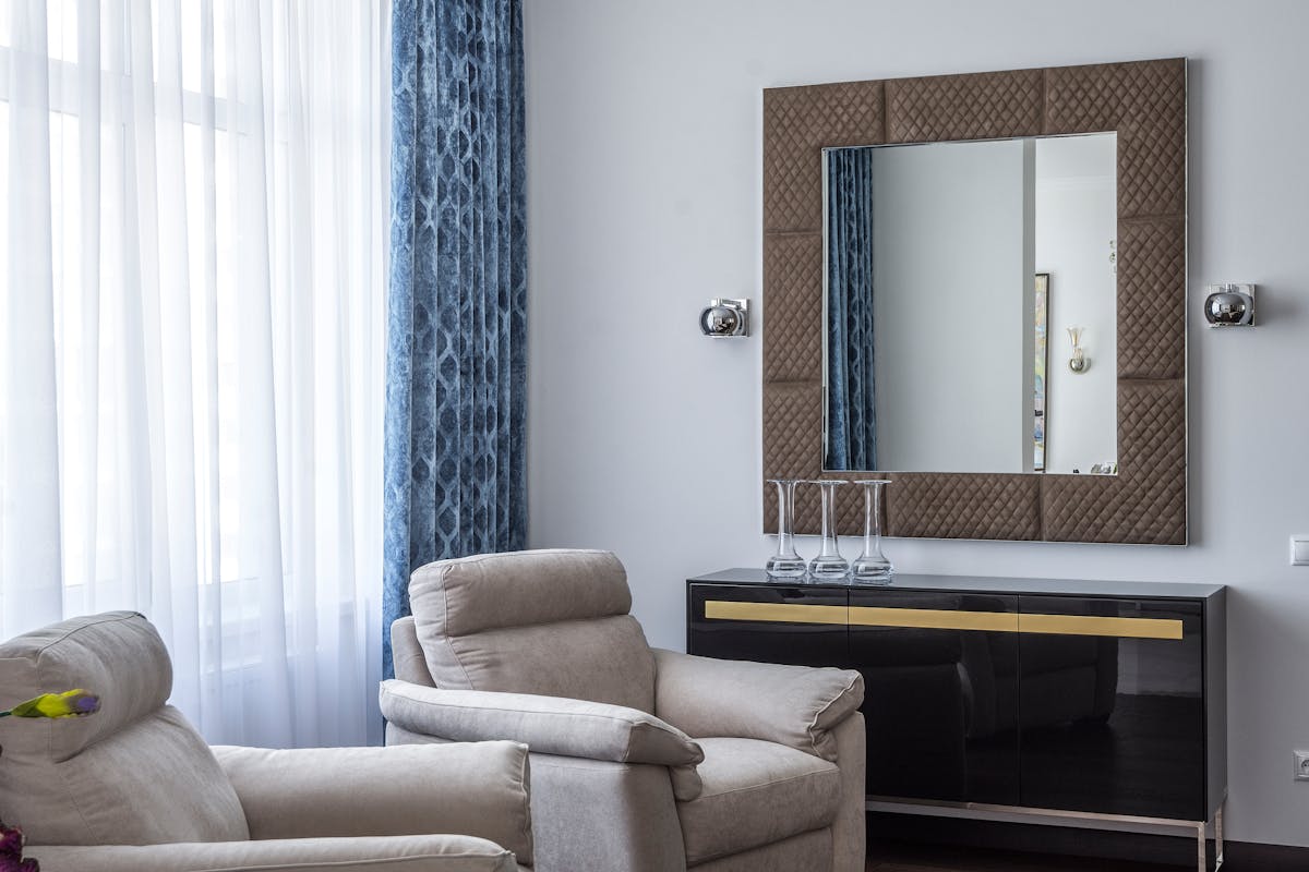Modern living room with armchairs and a large square framed mirror, illustrating mirror frame and shape choices
