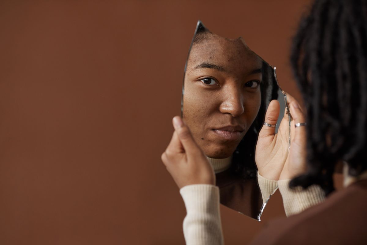 A woman holding and looking into a broken mirror reflecting on self image and fractured identity representing literary symbolism of shattered self-perception