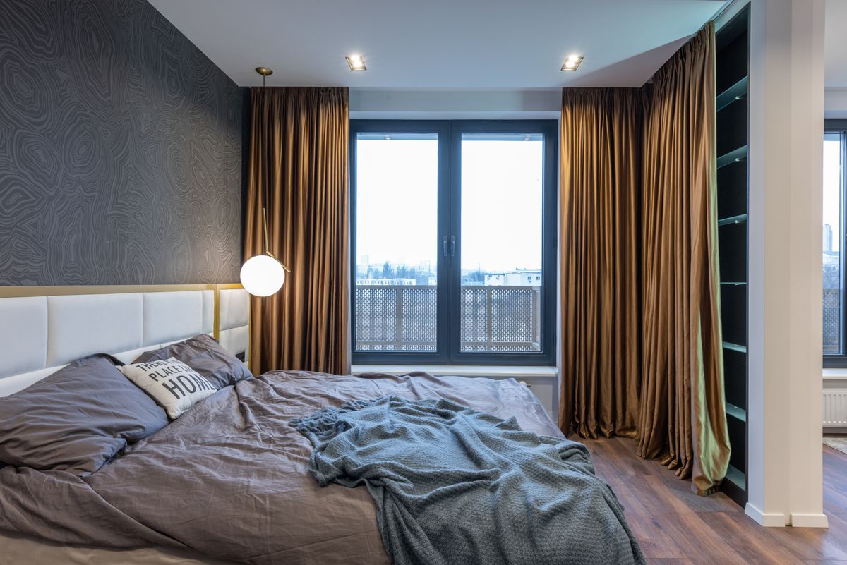 Calm bedroom with a soft bed beside a window dressed with curtains, illustrating heavy curtains as a feng shui cure