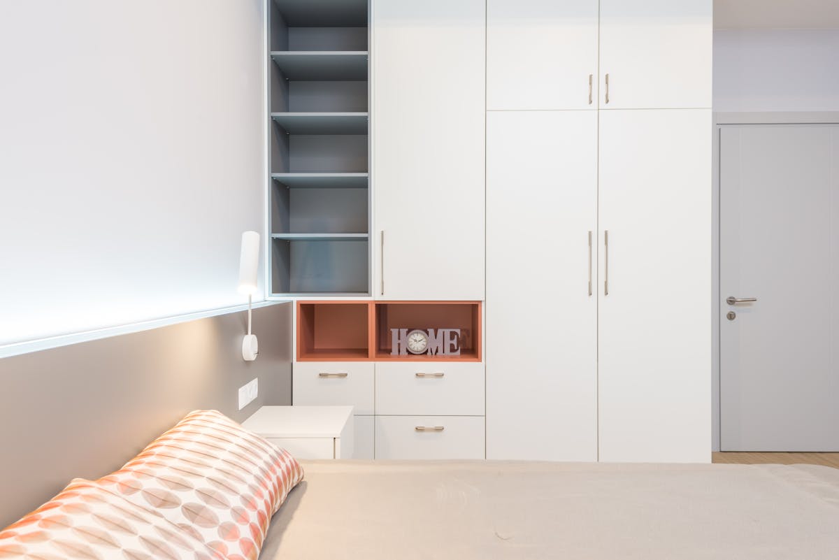 White wardrobe beside a bed illustrating feng shui bedroom furniture placement White wardrobe and storage placed against the wall beside a bed, illustrating feng shui bedroom furniture placement